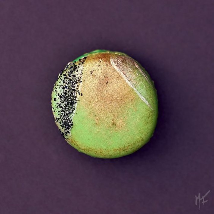 photograph of a green and gold macaroon on a purple background, visual storytelling by marco joe fazio