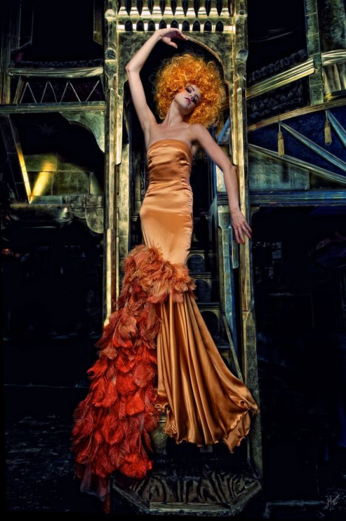 Beautiful women in an orange silk gown with orange curly hair posing in a gold architectural setting, visual storytelling by marco joe fazio