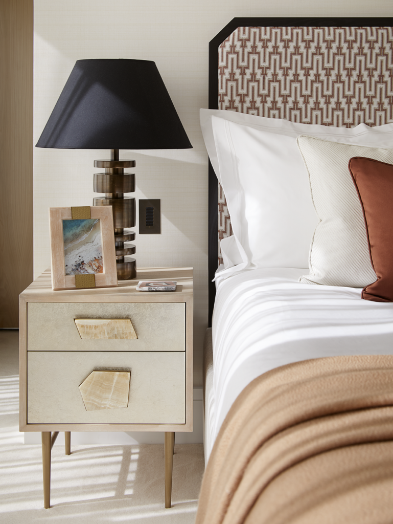 A cream nightstand with stone handles and a bronze bed in a Playful Interior by Elycion