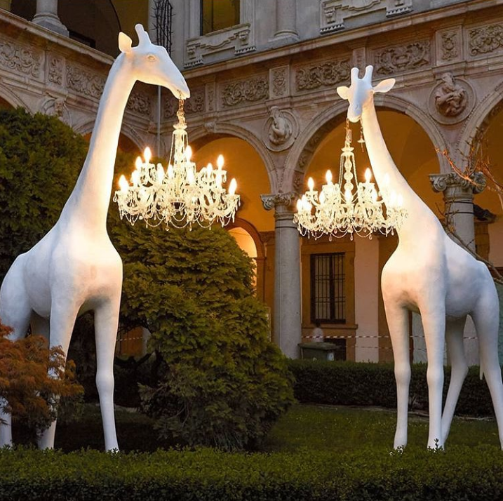 large giraffe statues with chandeliers hanging from their mouths - giraffes in love installation by marcantonio, qeeboo and masiero lights during milan design week 2019