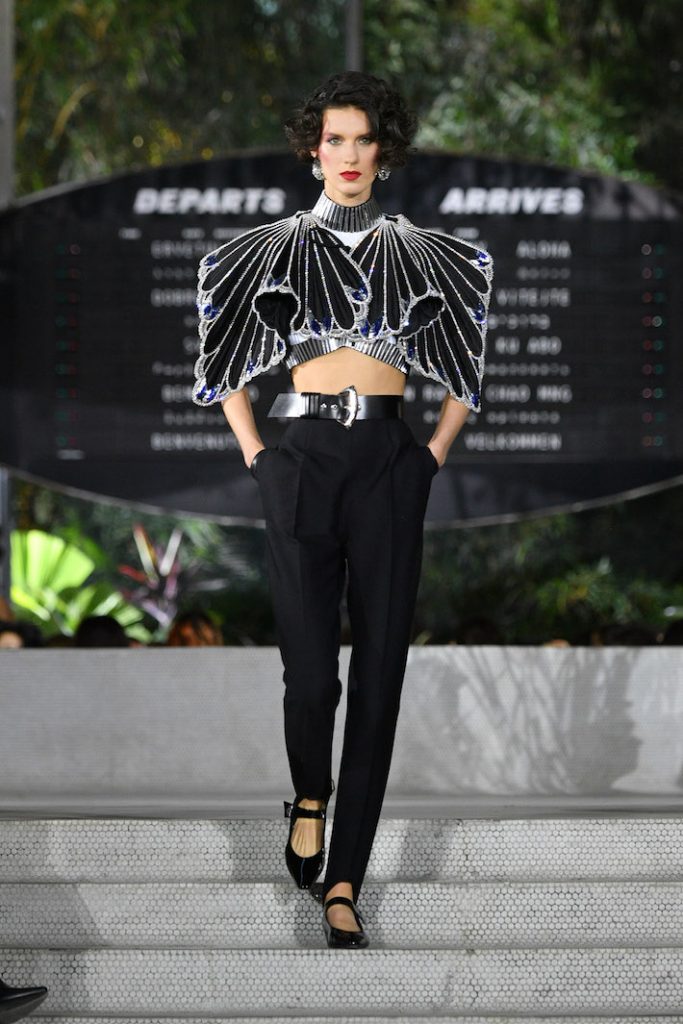 Model walks the runway during the Louis Vuitton Cruise 2020 Fashion Show wearing a dramatic crop top and black skinny pants