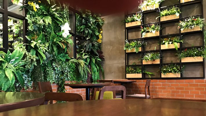Empty wood table with artificial plant decoration on the wall of coffee shop ecology design interior. Fake tree from plastic plants ornamental design on the wall of green office.