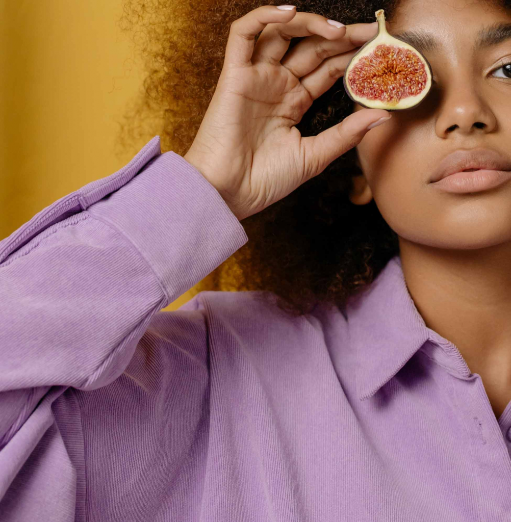beautiful woman holding a fig by her eye