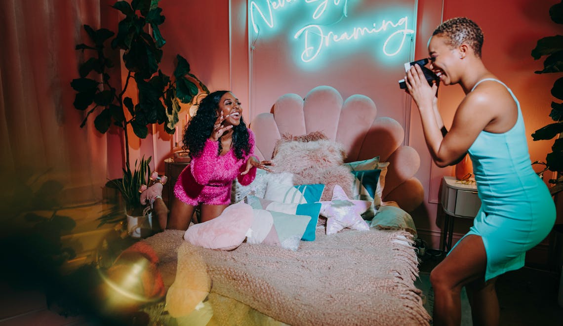 Two friends enjoy a vibrant indoor photoshoot with neon lights and playful decor.