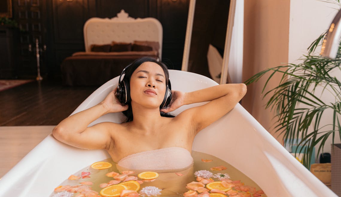 Woman enjoys a soothing floral bath, listening to music with headphones for ultimate relaxation.