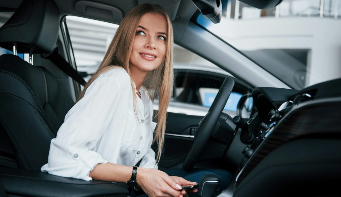 blonde woman sitting in a car holding a phone and smiling