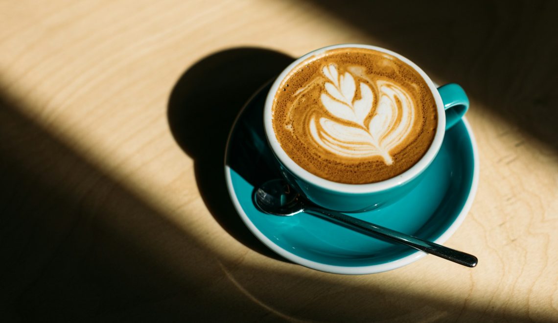 A cup of a cappuccino on a saucer with a spoon