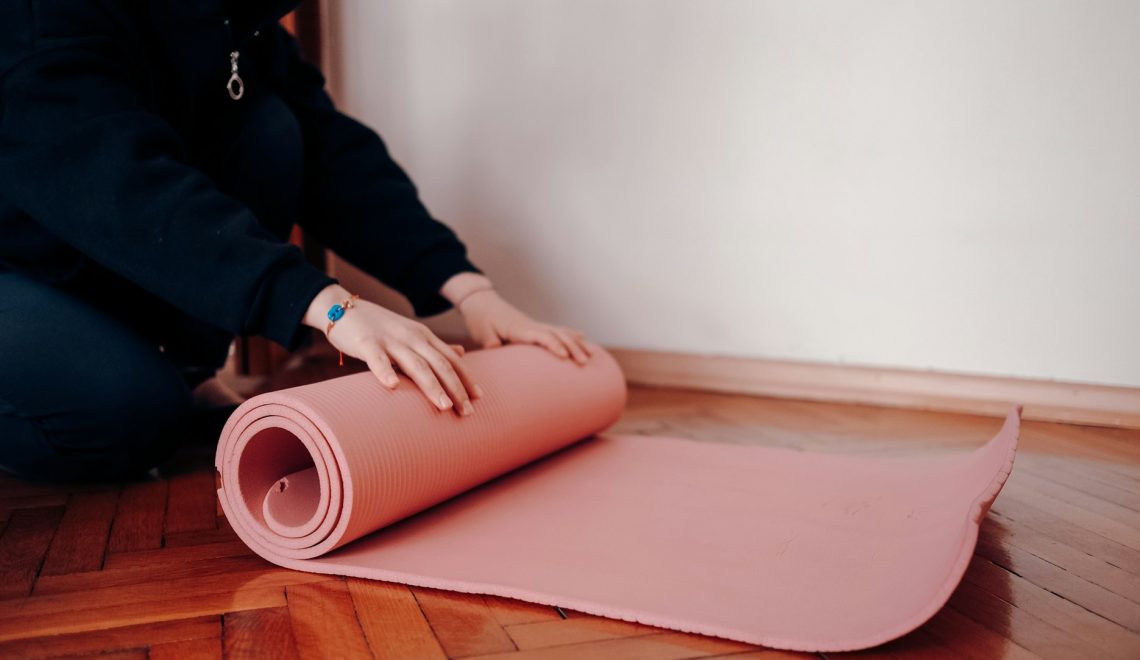 Person rolling up a pink mat on the floor
