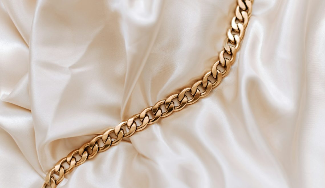 A gold cuban link chain on a satin background