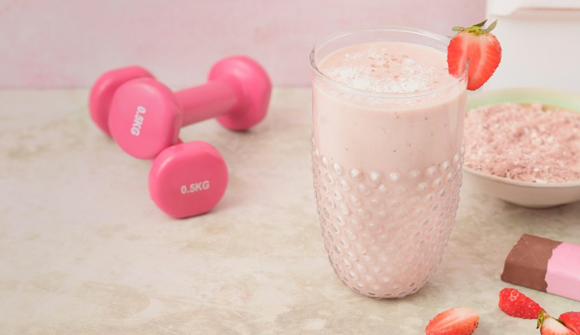 a glass of strawberry supplement and two dumbbells