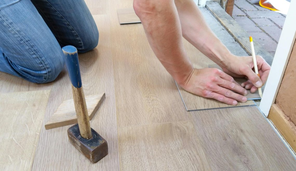 A person installing wooden flooring, carefully measuring and marking a plank near a doorway