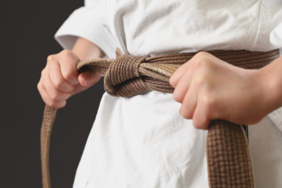 Close-up of a person tying a brown martial arts belt over a white uniform