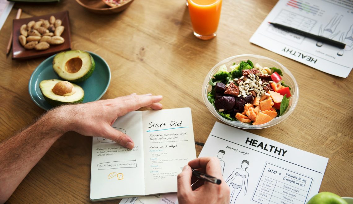 Person planning a healthy diet at a table with fresh food, salad, juice, and nutrition notes