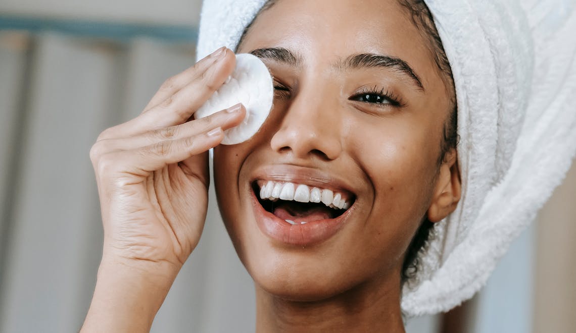 woman smiling and using a cotton pad on her face