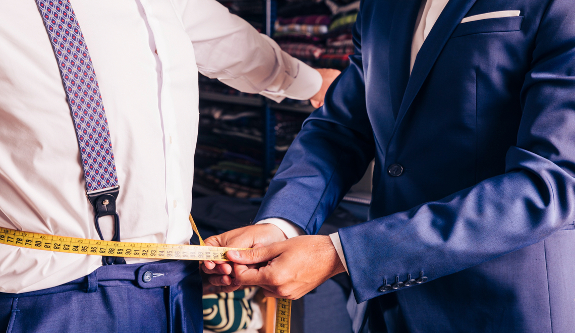 male tailor taking measurement of man's waist