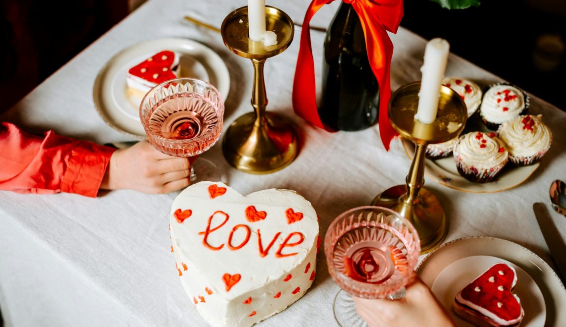 Una torta a forma di cuore, pasticcini e due bicchieri sopra un tavolo
