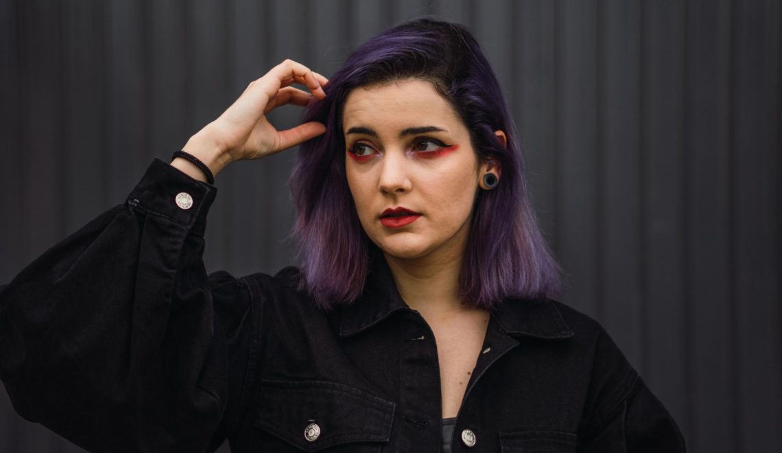 Portrait of a woman with purple hair and red lipstick on the black wall background