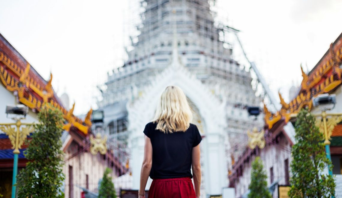 Woman standing in front of a traditional Asian temple with ornate architecture and golden details