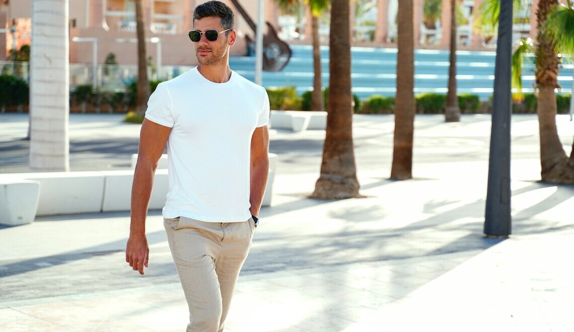 Man walking confidently in a casual outfit with a white T-shirt and beige pants on a sunny day