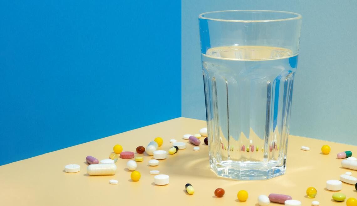 glass of water with pills surrounding it