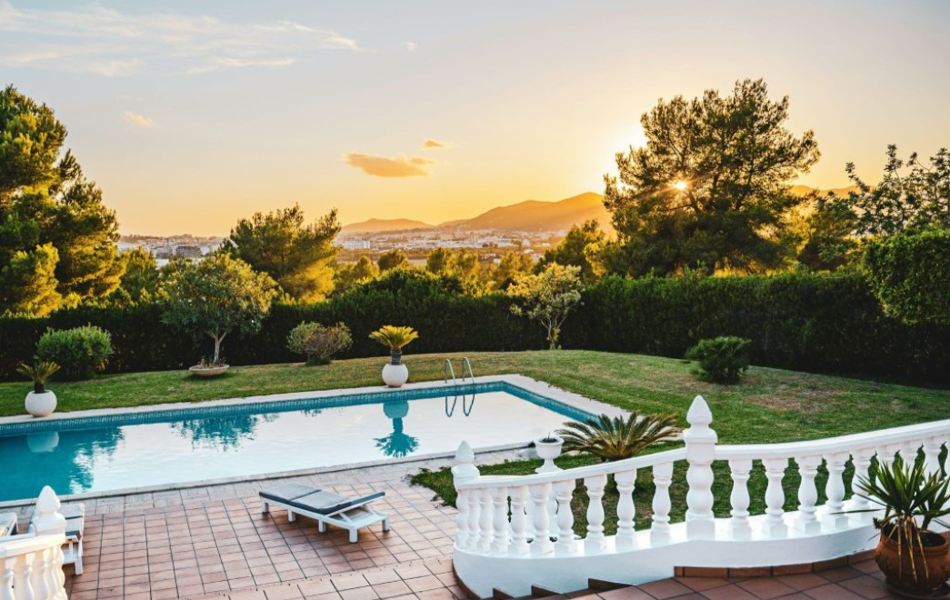 Luxury villa backyard with a swimming pool, tiled patio, and lounge chairs overlooking a scenic mountain valley at sunset.