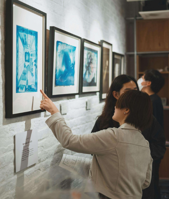 Visitors viewing framed blue cyanotype artwork at an art gallery exhibition