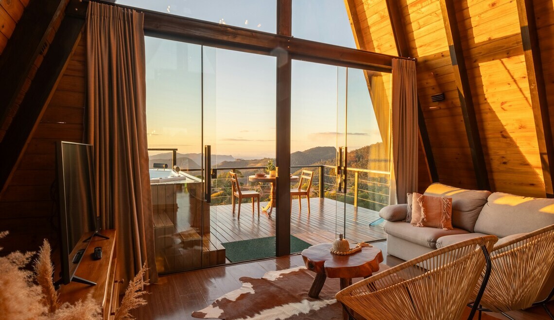 A-frame cabin with glass doors opening to a mountain-view deck at sunset.