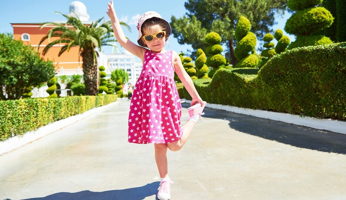 portrait of a happy child wearing a pink dress, hat and sunglasses