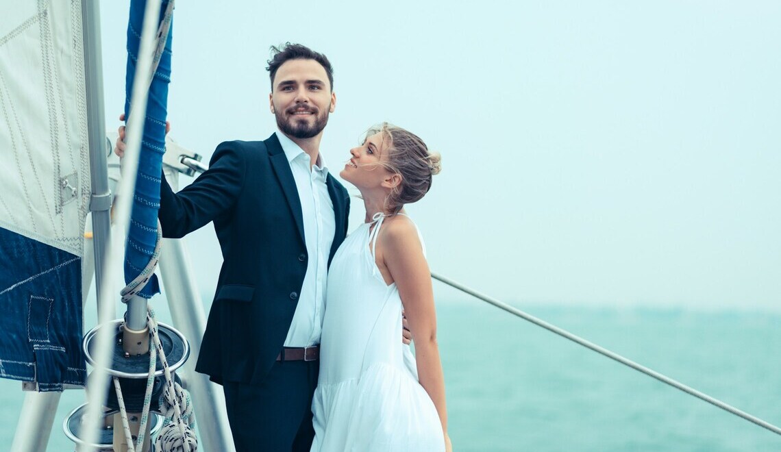 Un uomo in giacca e cravatta e una donna in abito bianco in piedi su una barca a vela