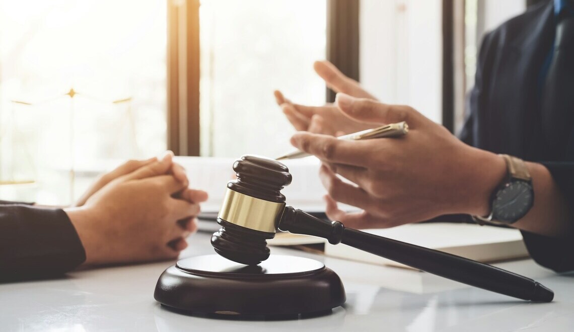 Wooden judge's gavel on a desk with people talking in the background.