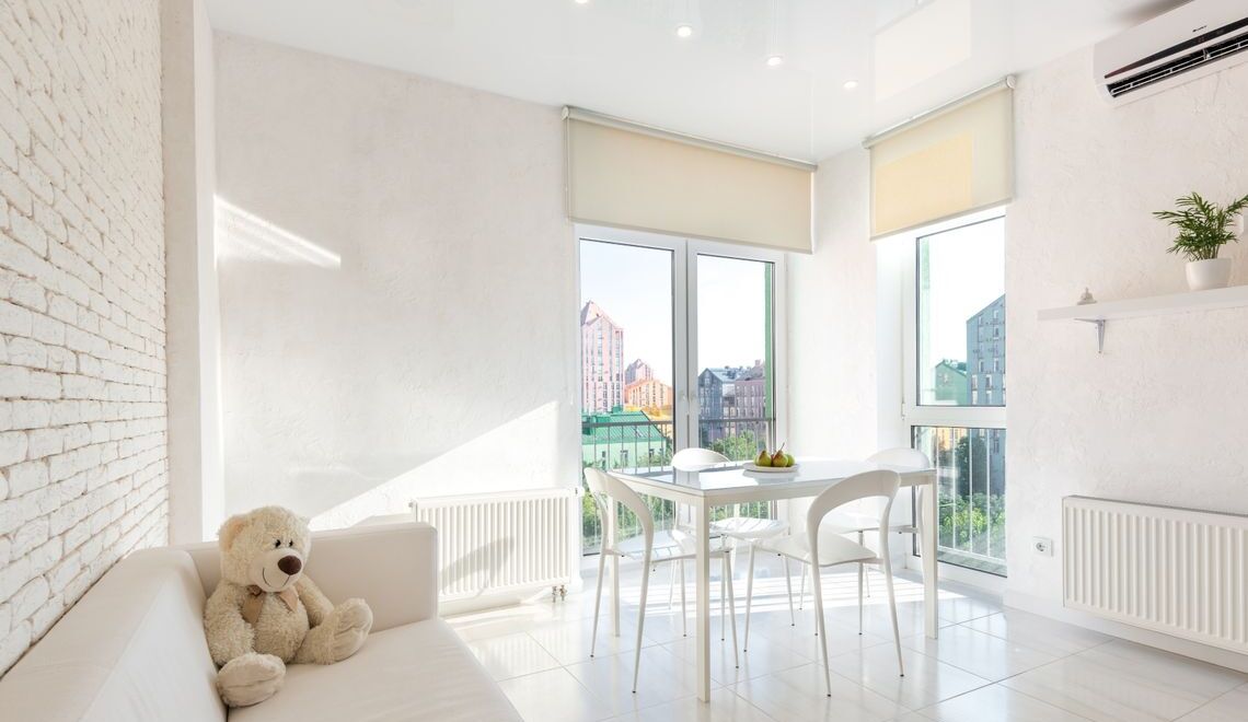 Contemporary bright white living space with a teddy bear on a sofa, dining table, and large windows
