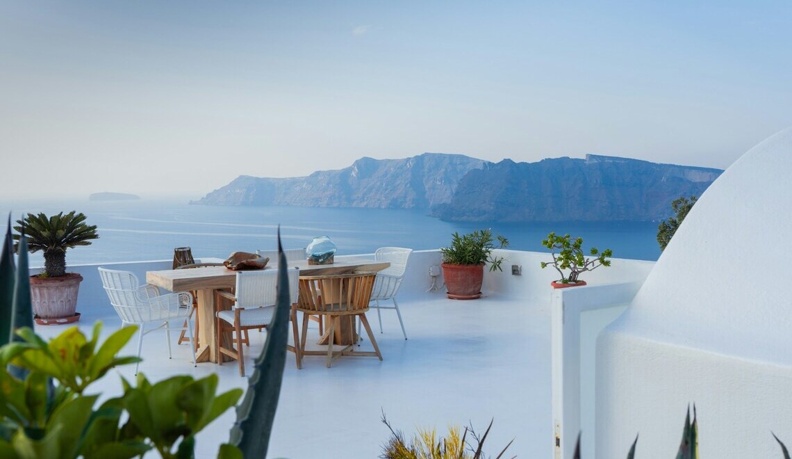 Tavolo da pranzo all'aperto su una terrazza bianca con vista sul mare e sulle montagne di Santorini