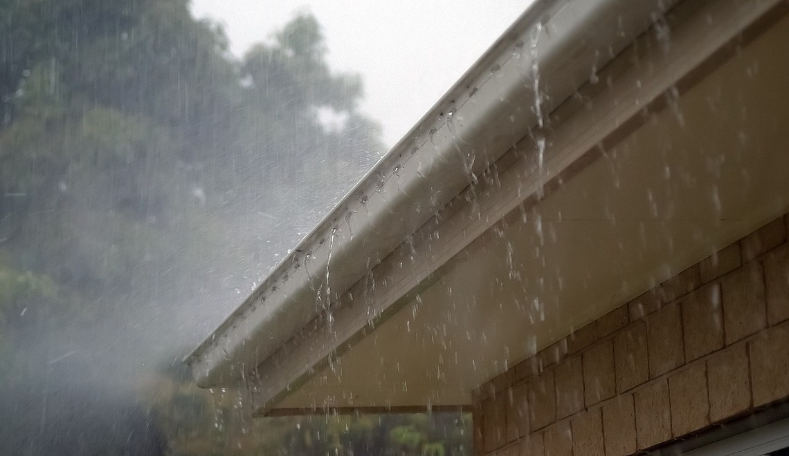 Heavy rain pouring and overflowing from a house roof gutter