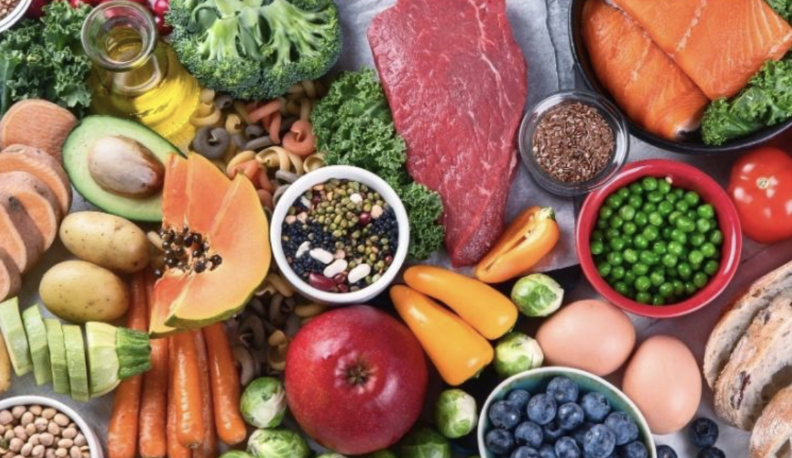 A colorful overhead shot of various healthy foods, including meat, fish, fruits, and vegetables