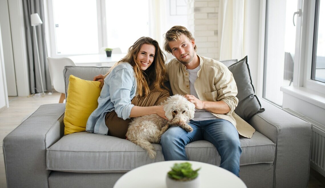 couple sitting on a couch in a bright living room petting their dog