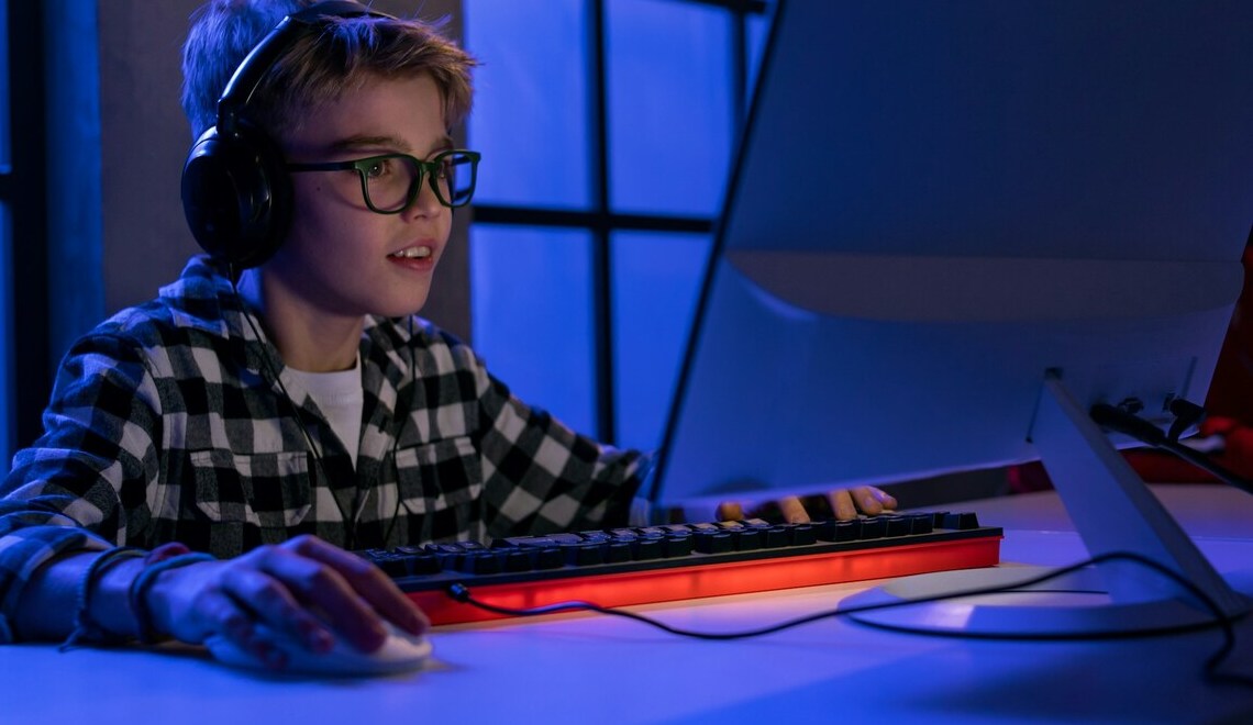 Young boy with glasses and headphones playing video games on a computer