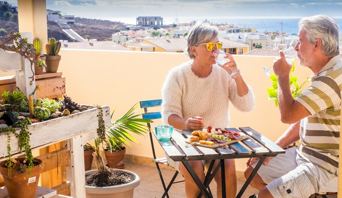 Senior couple enjoying drinks and snacks on a sunny balcony