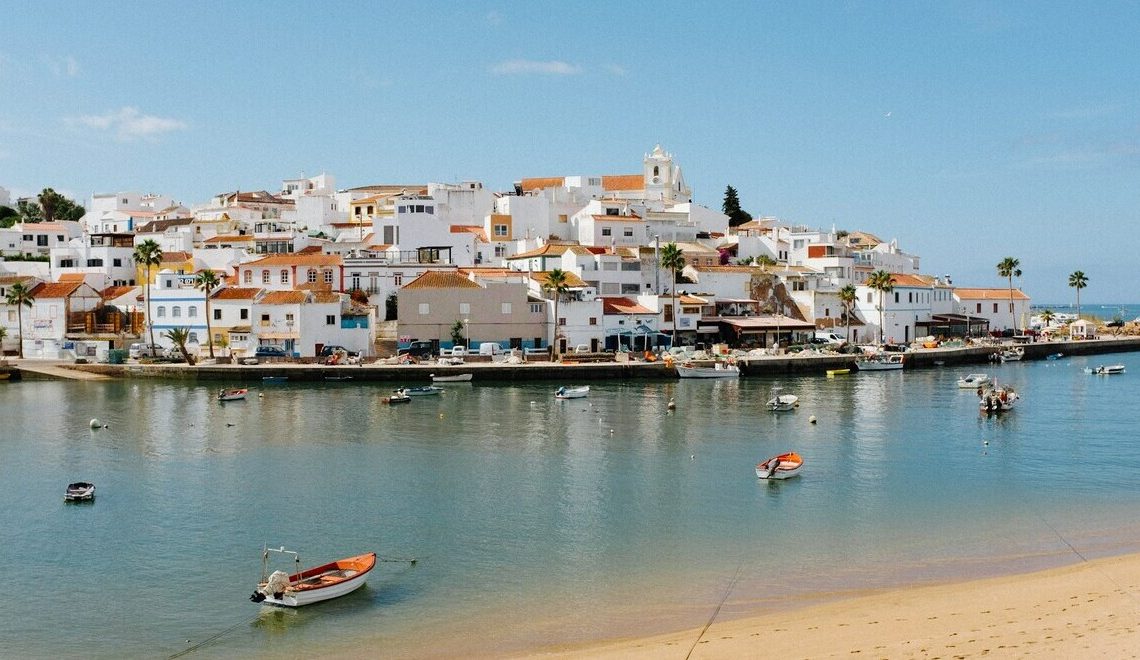 Scenic view of a coastal village with whitewashed buildings and boats on calm water in Algarve, Portugal