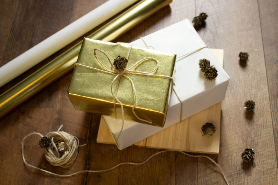 Wrapped gift boxes in gold and white paper tied with twine and decorated with small pine cones on a wooden surface.