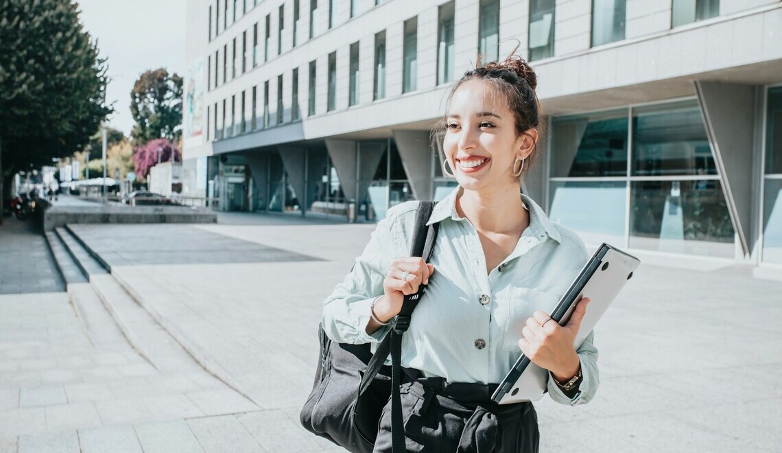 Smiling woman holding a laptop while walking outside