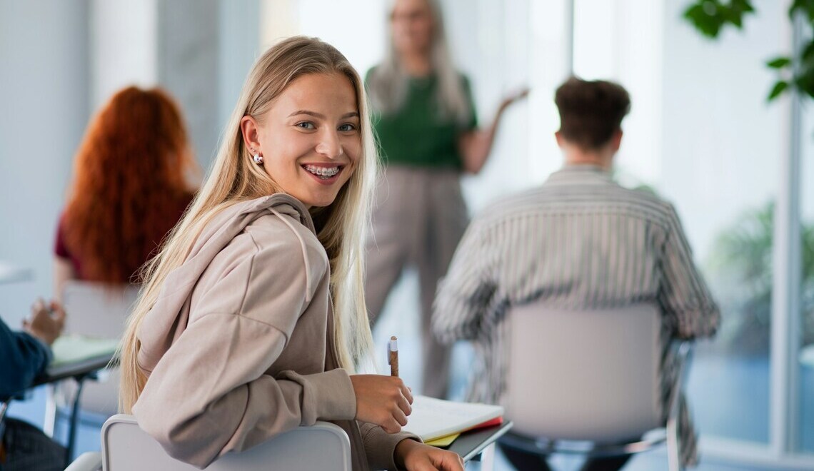 Smiling young woman with braces looking back over her shoulder during a classroom lecture