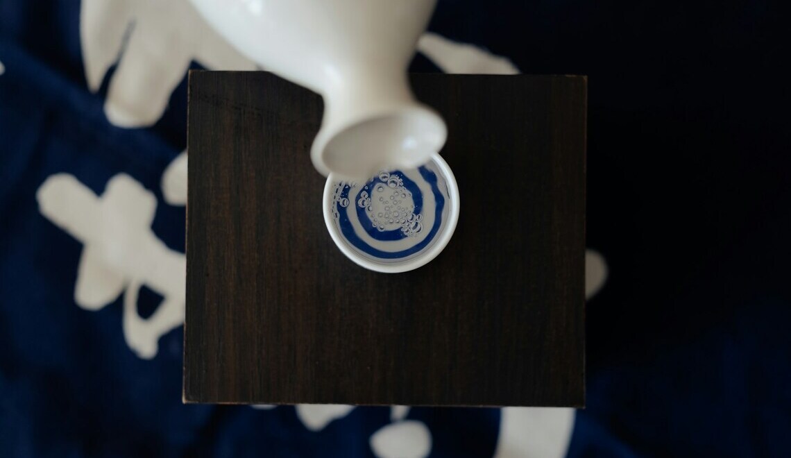 sake being poured from a white ceramic carafe into a small cup